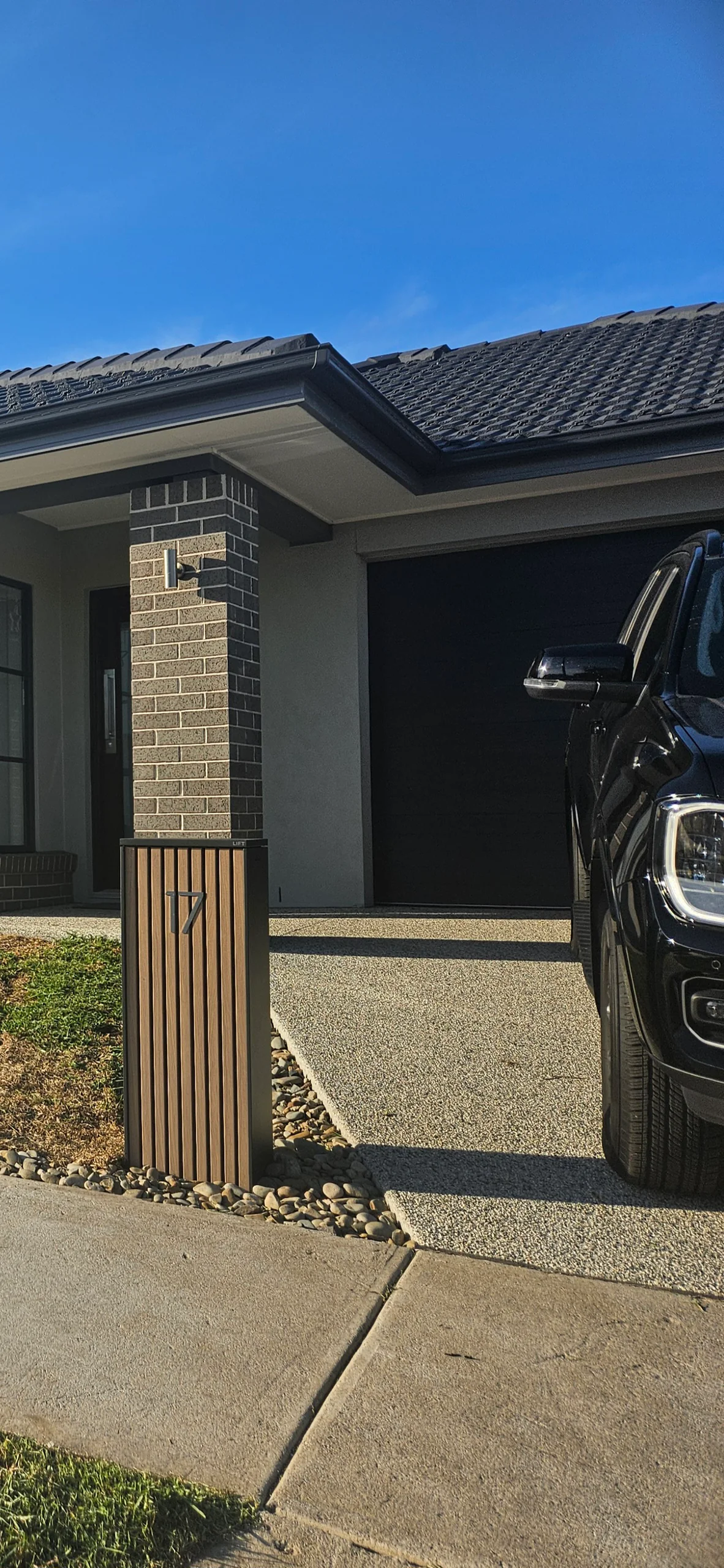 Modern charcoal letterbox with parcel drop set in a pebble bed